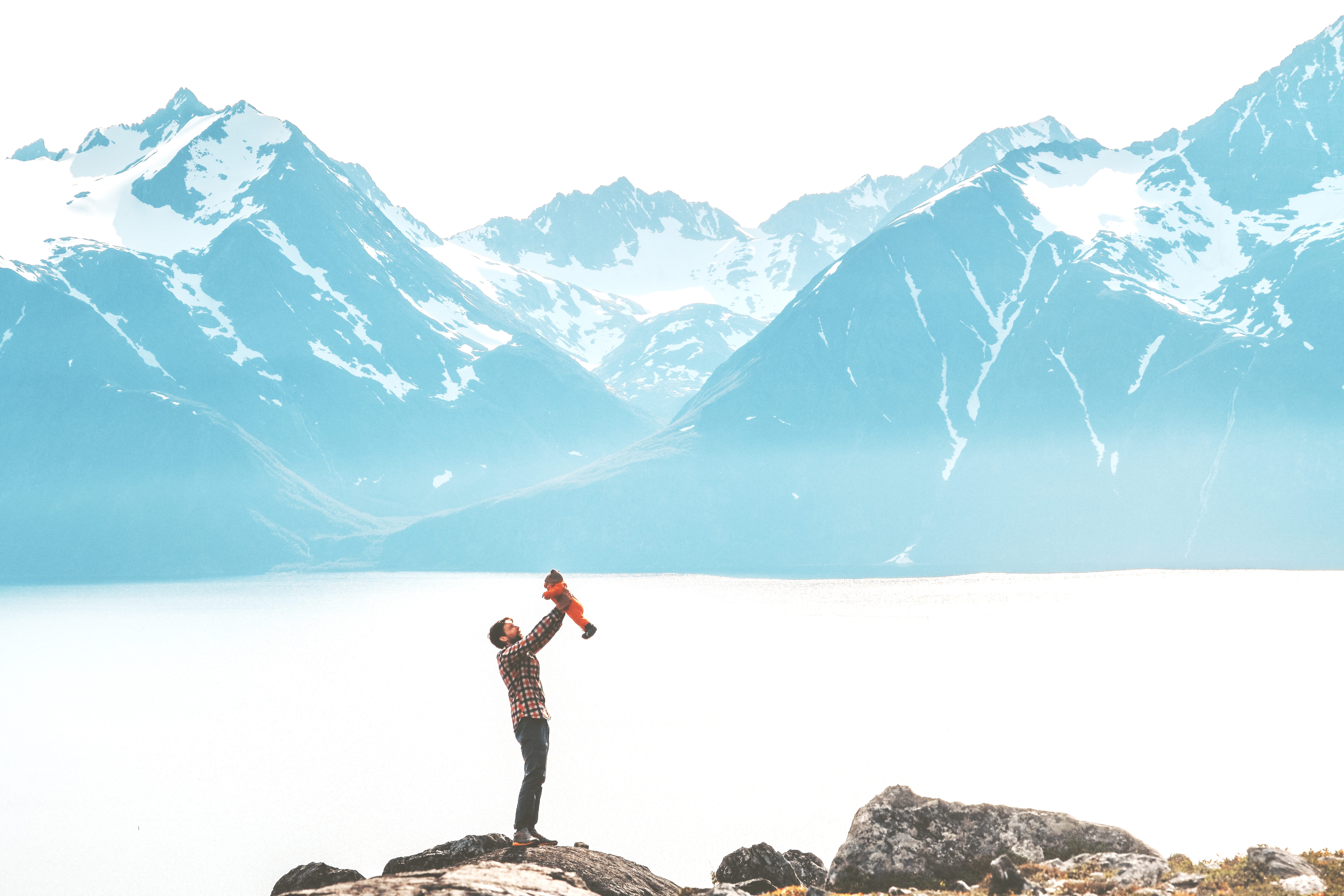 man lifting child proudly in the air in front of mountains
